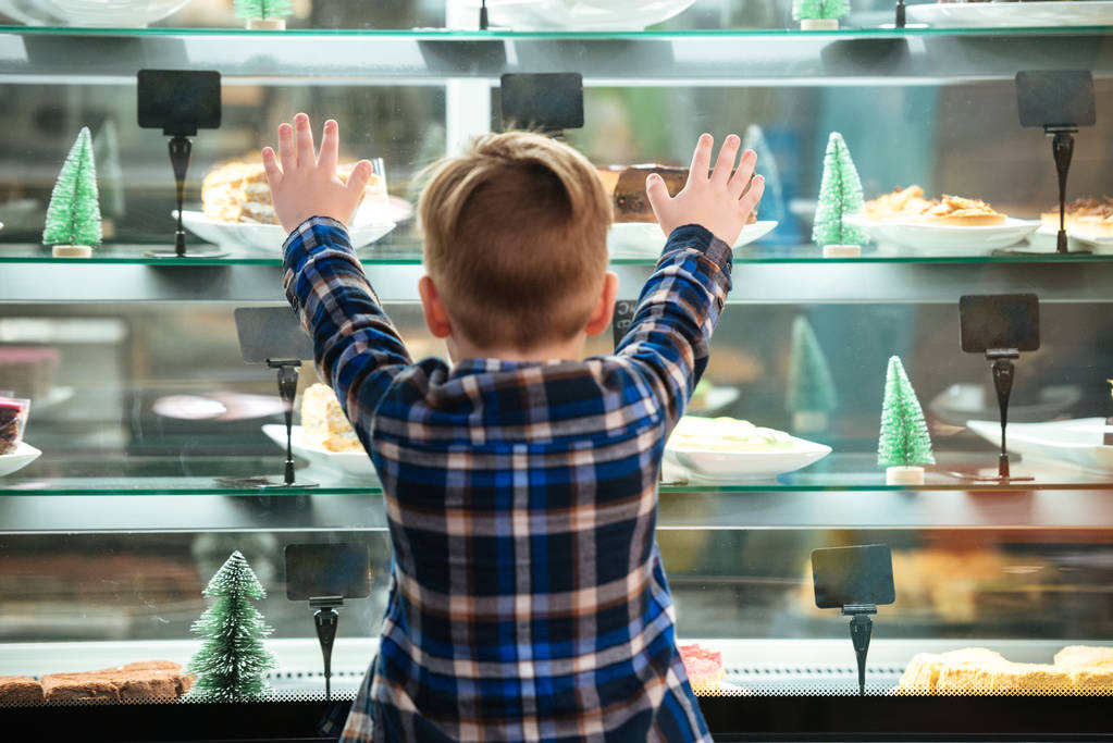 Вид сзади на маленького мальчика, смотрящего на торты на витрине
 - Фото, изображение