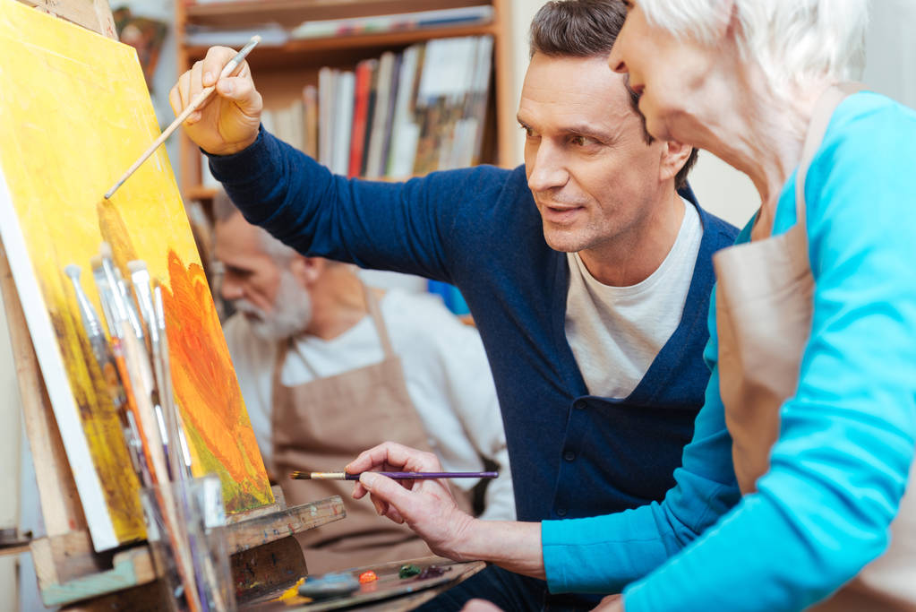 Artiste enchanté montrant aux femmes âgées comment peindre
. - Photo, image