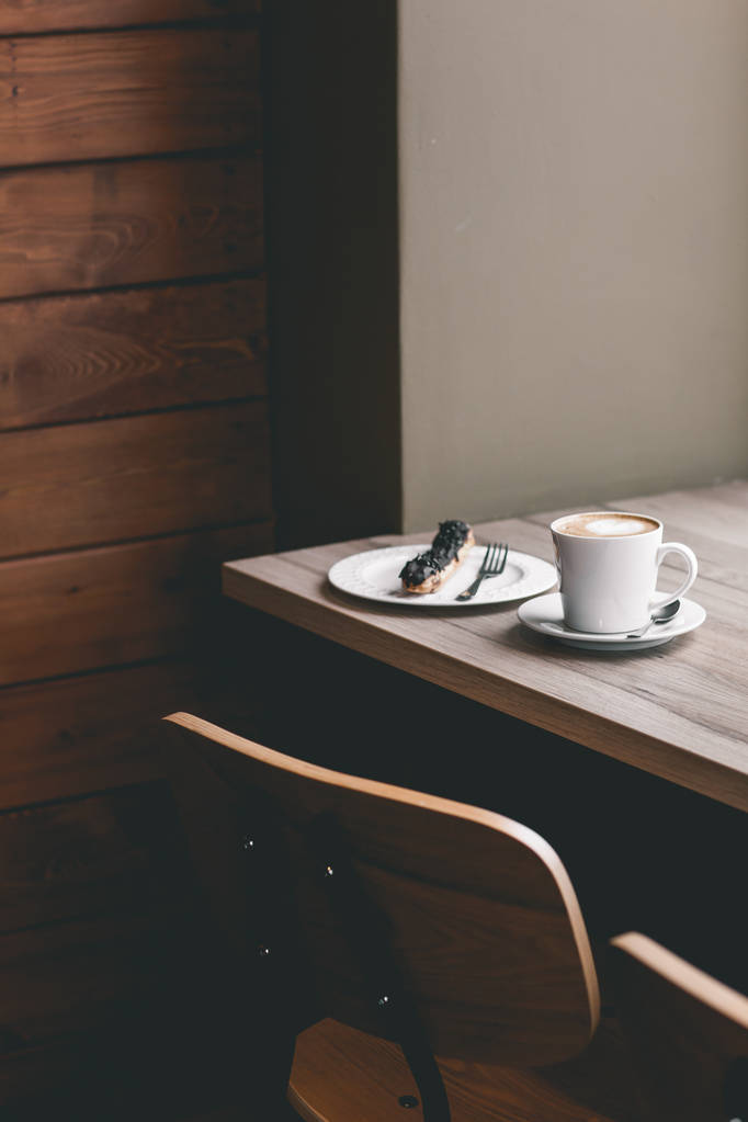 Xícara de café na mesa de madeira com eclair
 - Foto, Imagem