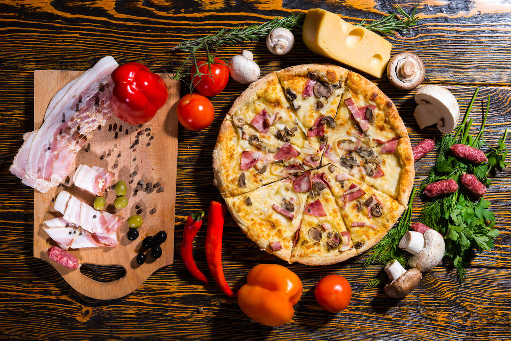 Hoge hoekmening van smakelijke pizza op houten tafel omringd door veg - Foto, afbeelding