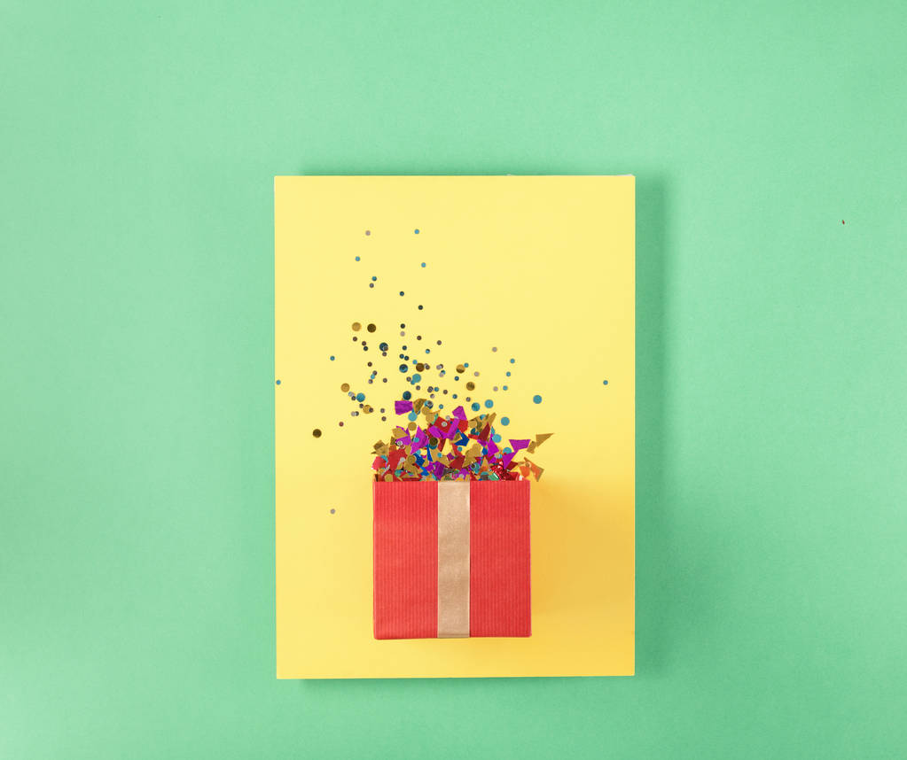 Coffret cadeau rouge avec divers confettis de fête sur carton jaune
 - Photo, image