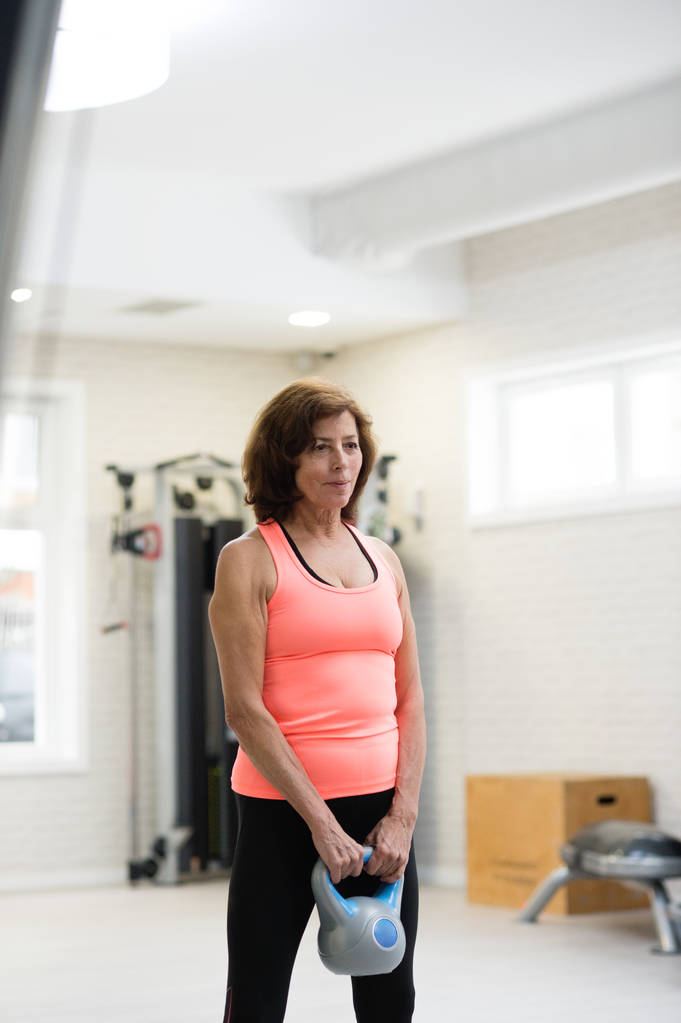 Mulher sênior no ginásio exercitando usando kettlebells
. - Foto, Imagem