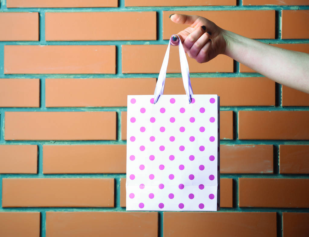 レンガの壁に女性の手で白い斑点を付けられたショッピング バッグ - 写真・画像