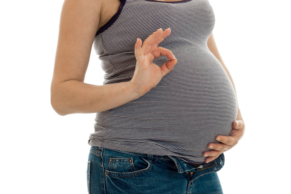 jovem mulher morena grávida com barriga grande posando e mostrando símbolo OK isolado no fundo branco
 - Foto, Imagem