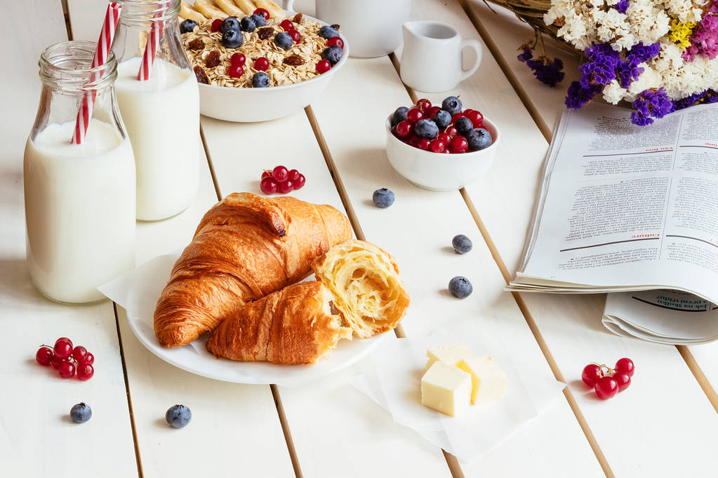 Sabroso desayuno con croissant, copos de avena, bayas y leche en la mesa de madera blanca
 - Foto, imagen