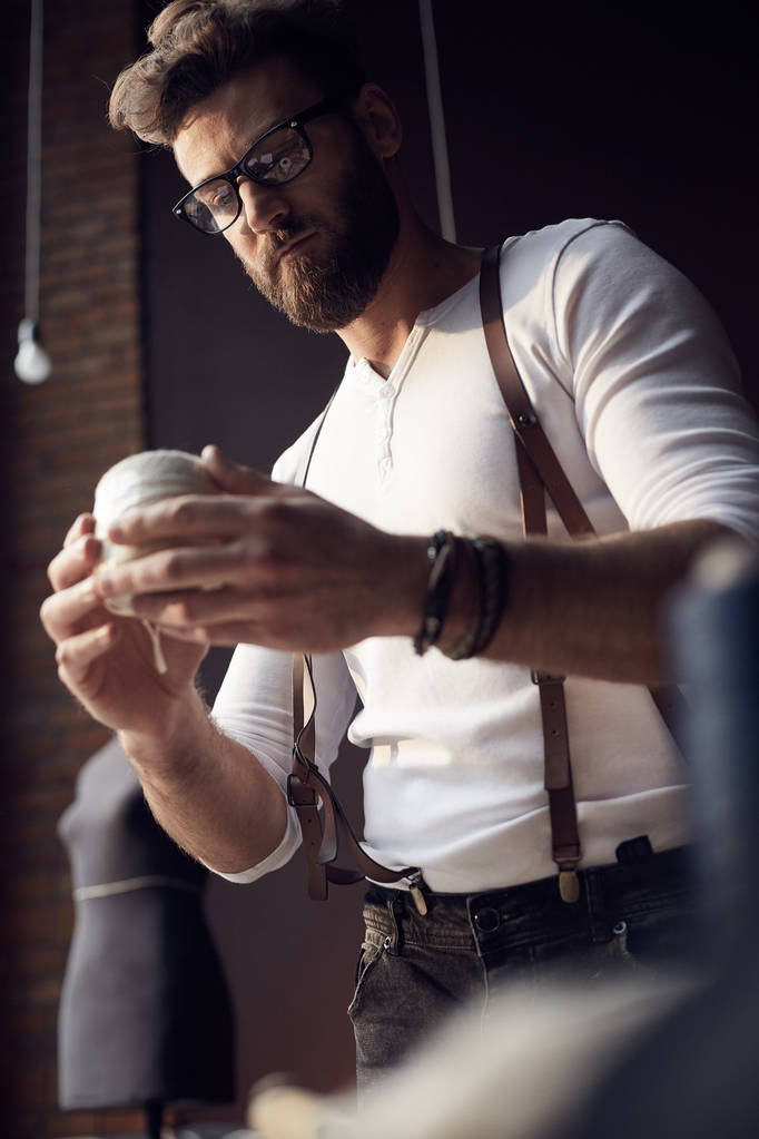 Krawiec przystojny mężczyzna z brodę i okulary w białej koszuli z brązowej skóry szelki pracujących w niesamowite atelier z zabytkowymi meblami i manekin na tle - Zdjęcie, obraz