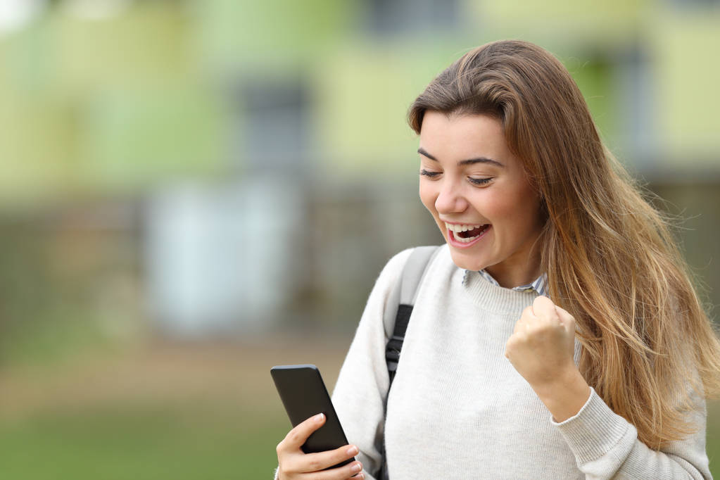 Ενθουσιασμένος φοιτητής ανάγνωση ειδήσεων σε ένα έξυπνο τηλέφωνο - Φωτογραφία, εικόνα