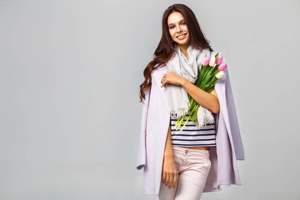 Photo de mode d'une belle jeune femme avec des tulipes à la main .elle habillée d'un beau manteau, écharpe, pantalon et T-shirt à rayures
 - Photo, image