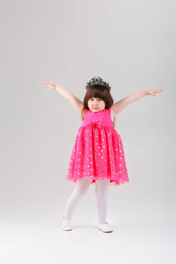 hermosa niña en vestido de princesa rosa con corona con brazo
 - Foto, Imagen