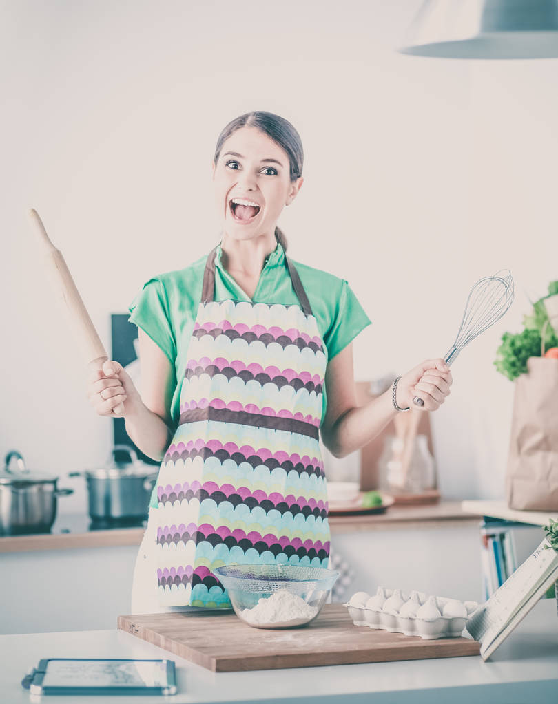 Χαμογελαστή νεαρή γυναίκα στην κουζίνα, απομονωμένη στο παρασκήνιο - Φωτογραφία, εικόνα