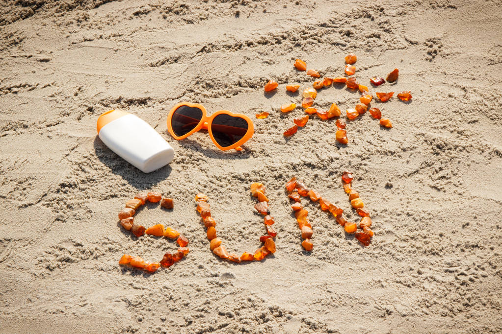 Word and shape of sun, sunglasses with sun lotion on sand at beach, summer time - Photo, Image