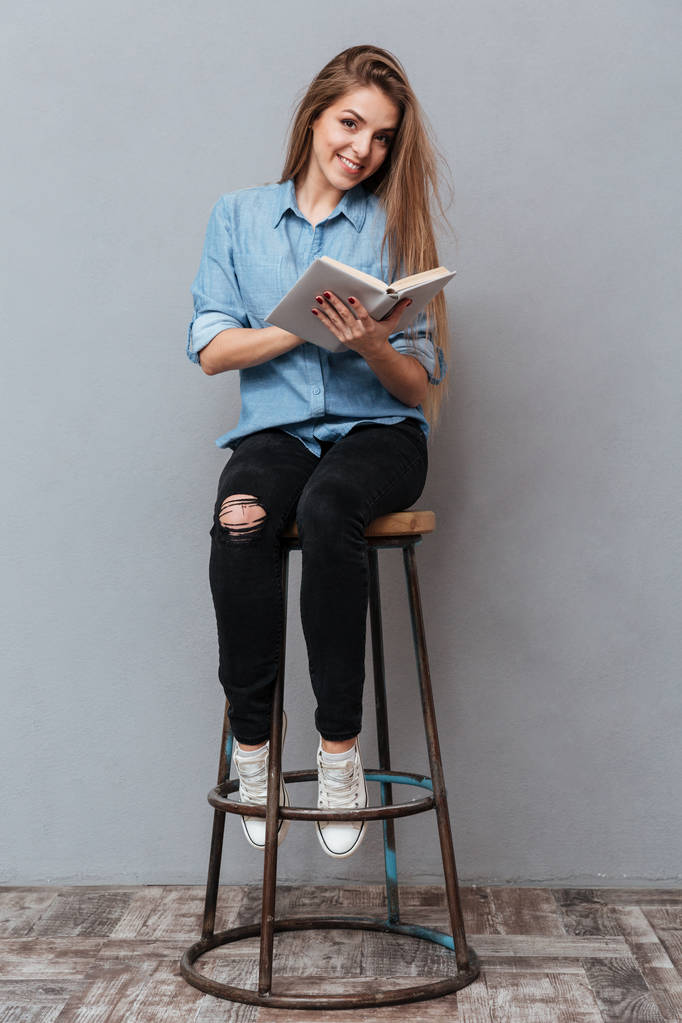Image verticale de la femme assise sur la chaise et le livre de lecture
 - Photo, image