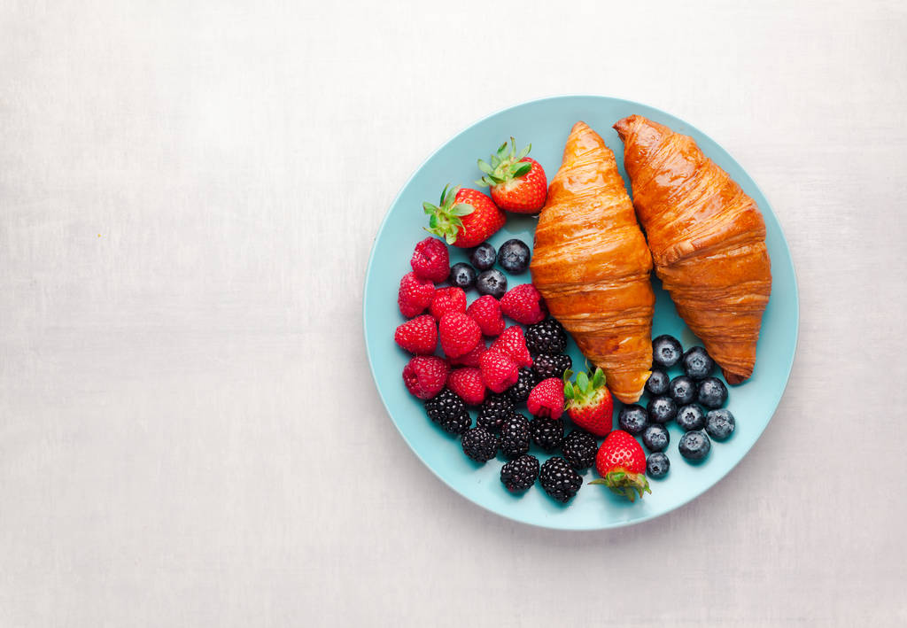 mixed berries and croissants on a blue plate on a white backgrou - Photo, Image