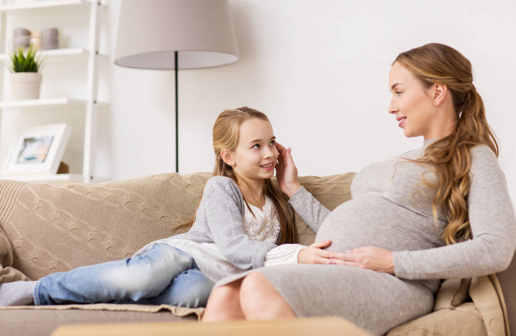 幸せな妊娠中の女性と自宅のソファの上の少女 - 写真・画像