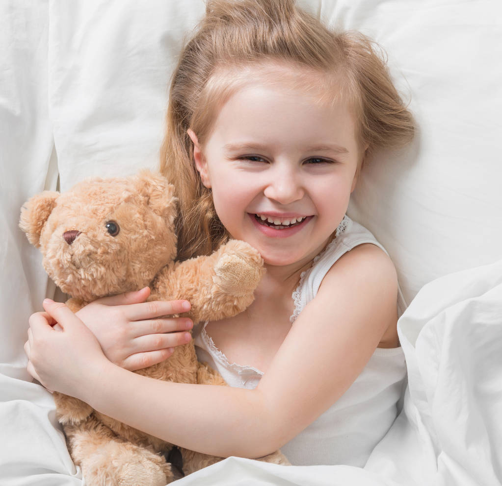 Dívka drží její hnědá teddy, v posteli - Fotografie, Obrázek