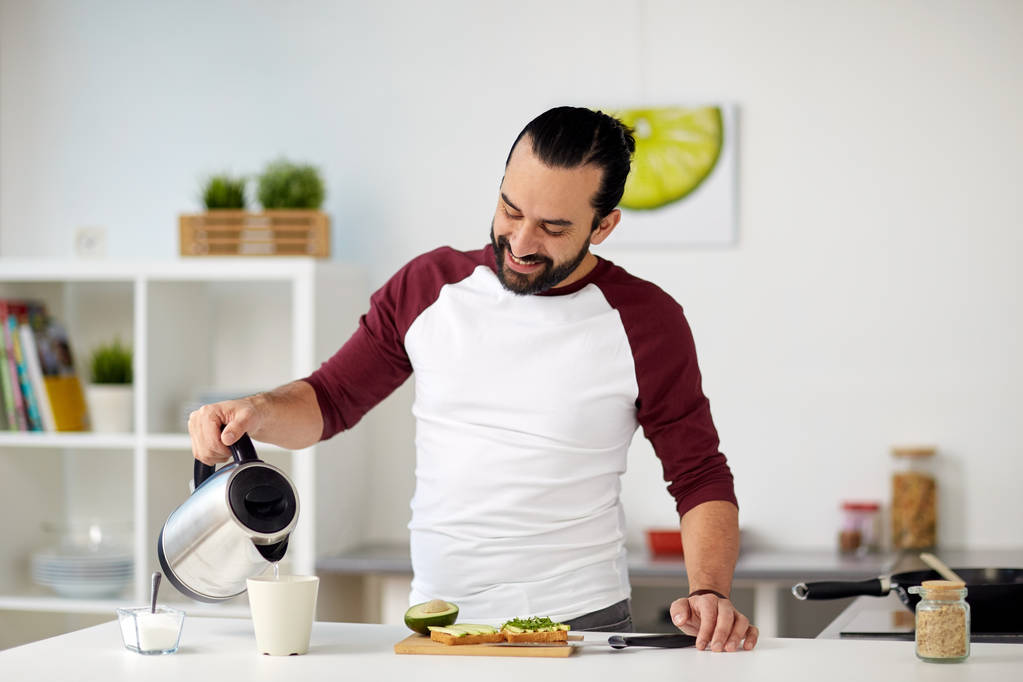 hombre con hervidor de agua haciendo té para el desayuno en casa
 - Foto, Imagen
