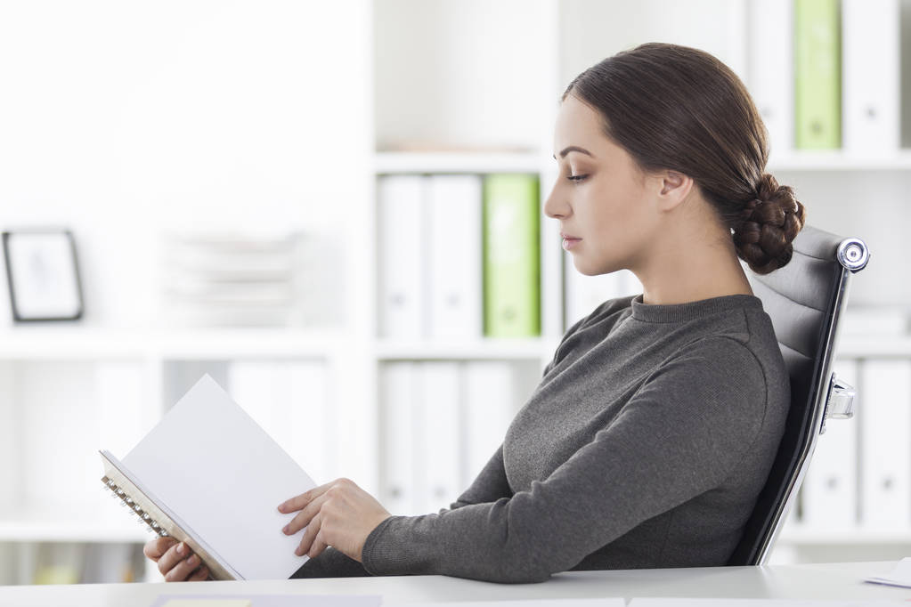 Zijaanzicht van de vrouw in grijze lezing in kantoor - Foto, afbeelding