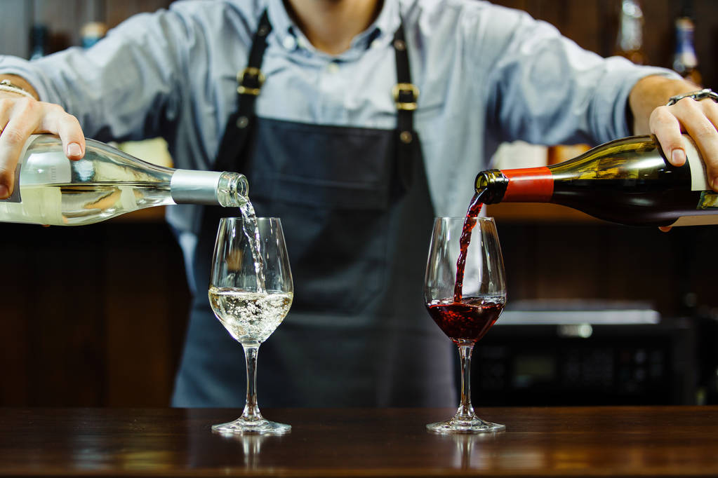 Sommelier masculino vertiendo vino tinto y blanco en copas de vino de tallo largo
 - Foto, imagen
