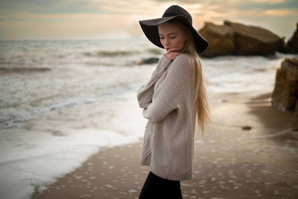 Жінка в капелюсі і светрі на зимовому пляжі на заході сонця
. - Фото, зображення