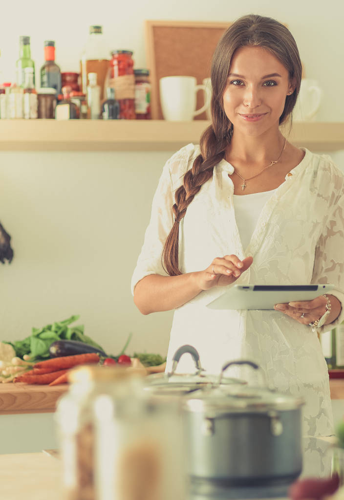 Giovane donna che utilizza un tablet per cucinare nella sua cucina - Foto, immagini
