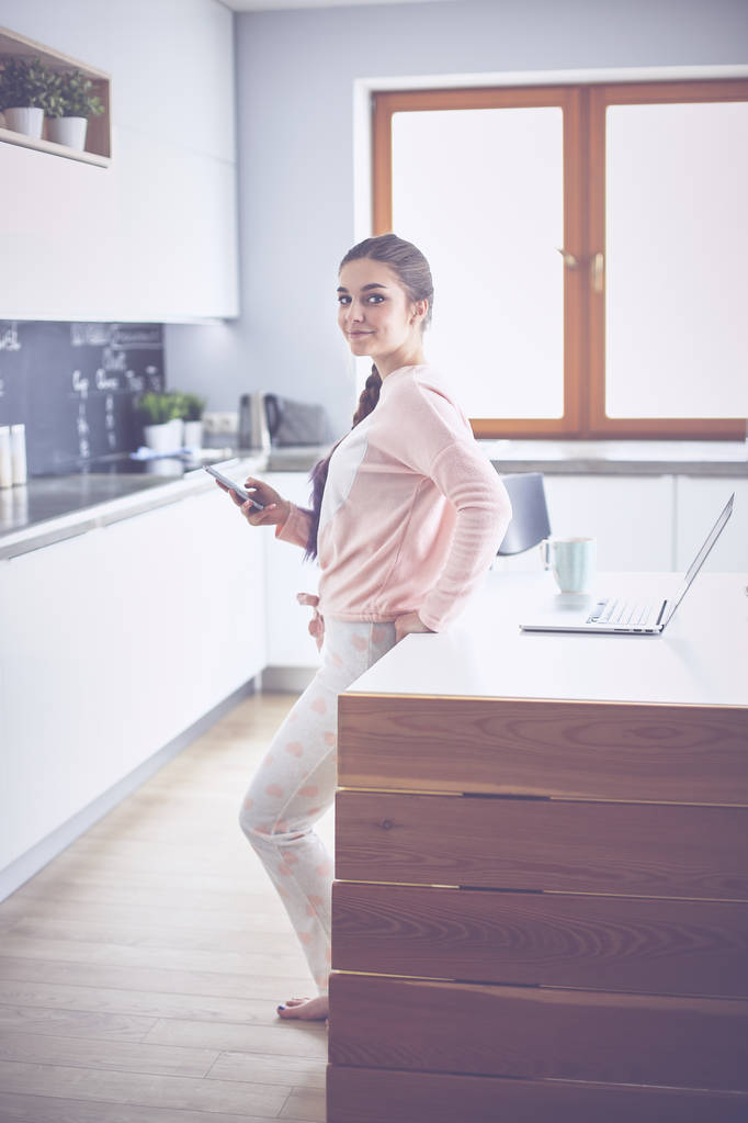 モダンなキッチンに立っている携帯電話をしている女の人 - 写真・画像