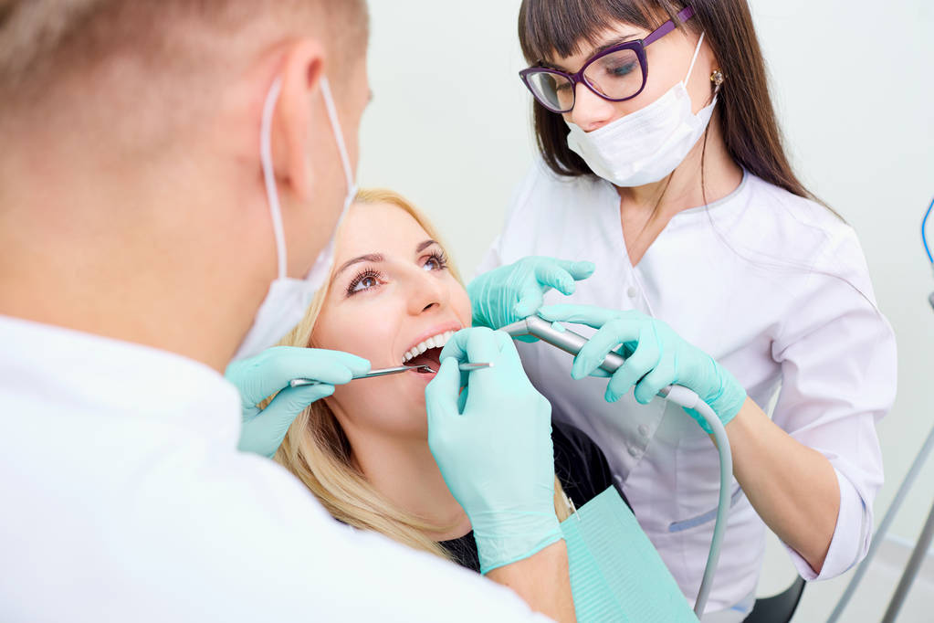 El dentista hombre y la mujer asistente están tratando los dientes a Clien
 - Foto, imagen