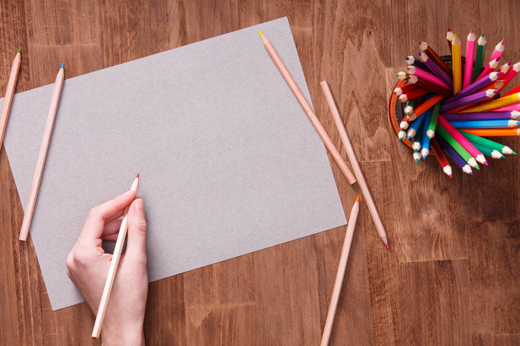 Dívka ruka kreslení, prázdný šedý papír a barevné tužky na dřevěný stůl - Fotografie, Obrázek