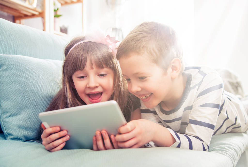 Happy sourozenci leží na pohovce doma a hrát spolu s tabletem - Fotografie, Obrázek