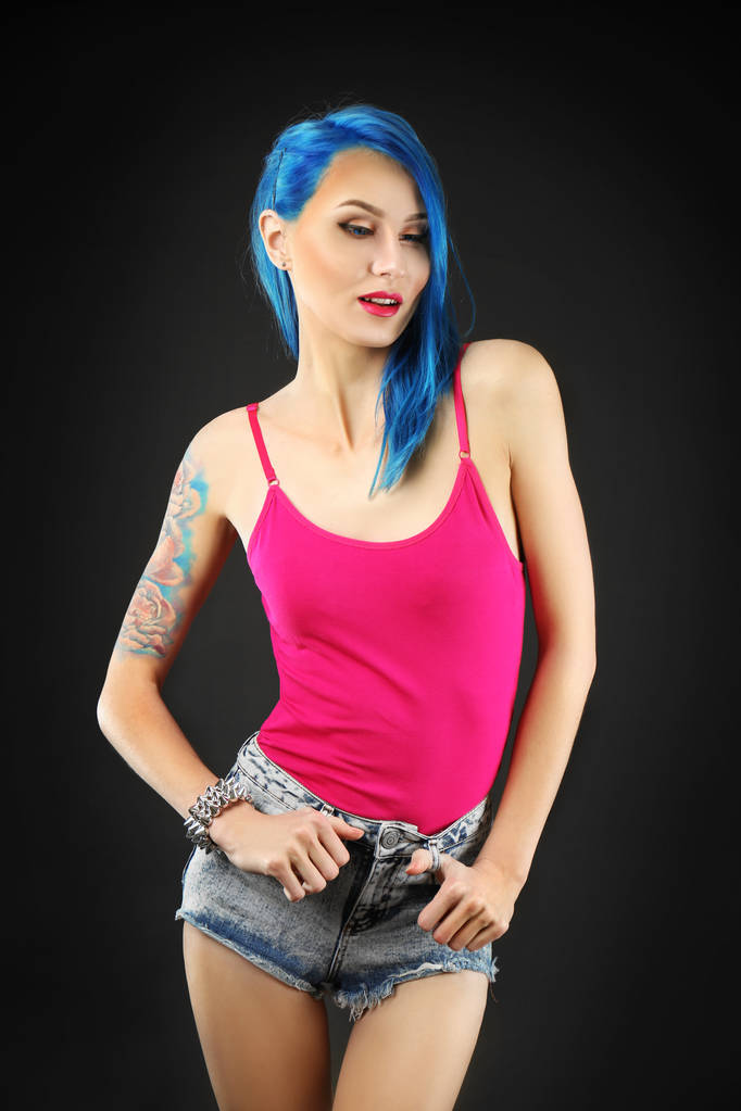 Beautiful young woman with stylish color hair and tattoo on dark background - Photo, Image