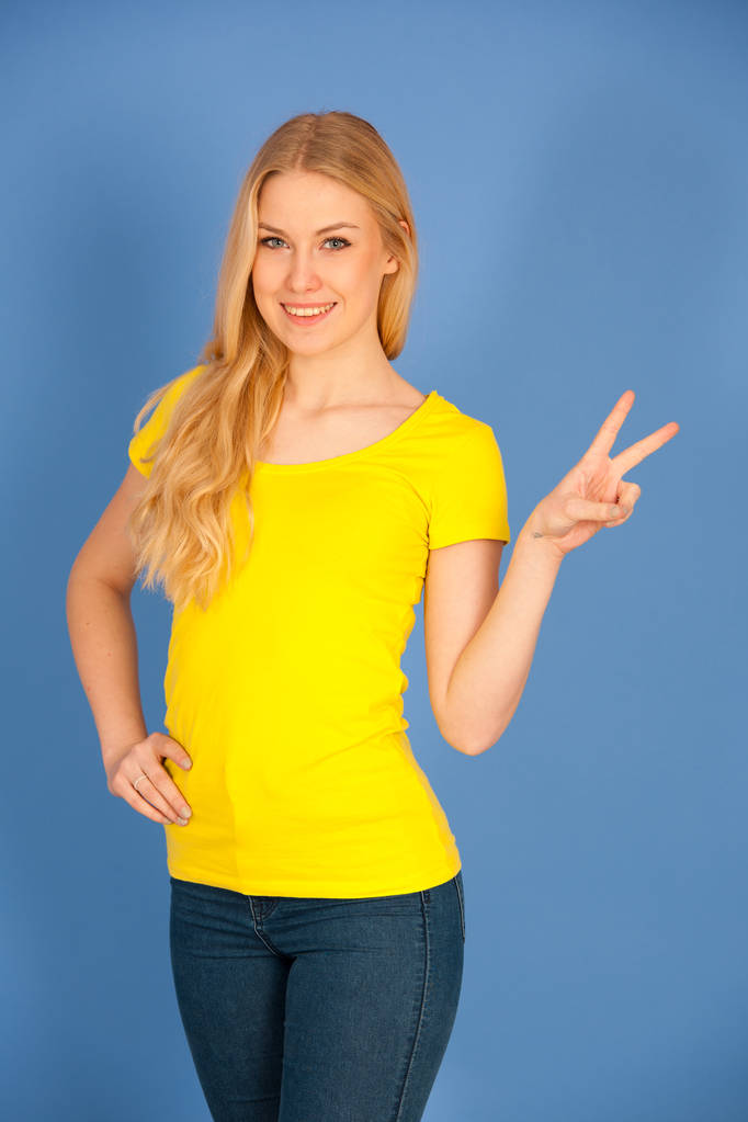 νεαρή ξανθιά γυναίκα στο κίτρινο t πουκάμισο νίκη χειρονομίες δείχνουν v  - Φωτογραφία, εικόνα