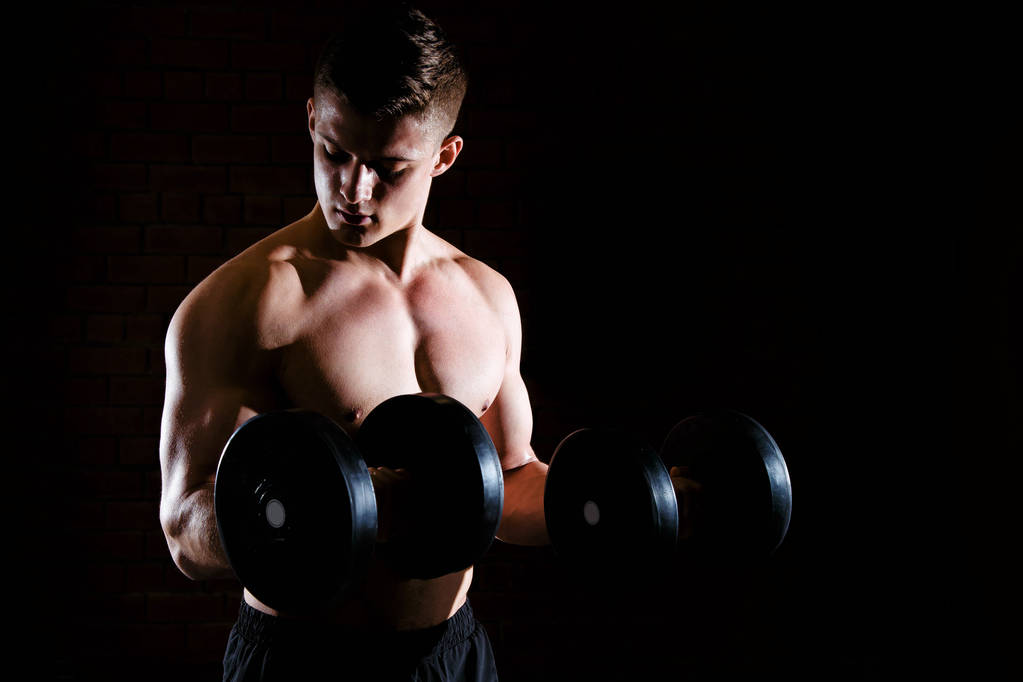 Nahaufnahme eines hübschen Powerathleten, der Muskeln mit Kurzhanteln hochpumpt - Foto, Bild