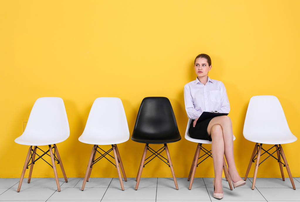 Mladá žena čeká na pracovní pohovor na žlutém pozadí zdi - Fotografie, Obrázek