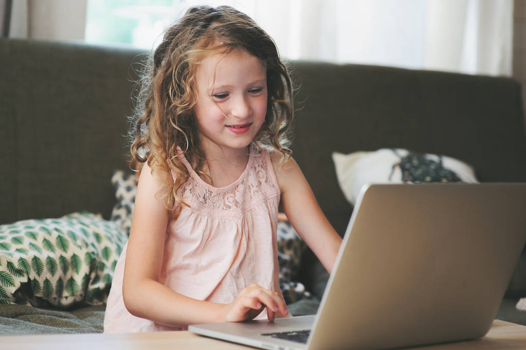 щаслива дитина використовує ноутбук вдома. Шкільна дівчина вчиться з комп'ютером та інтернетом в приміщенні
. - Фото, зображення
