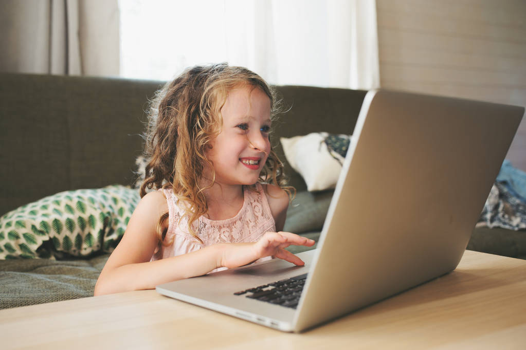 щаслива дитина використовує ноутбук вдома. Шкільна дівчина вчиться з комп'ютером та інтернетом в приміщенні
. - Фото, зображення