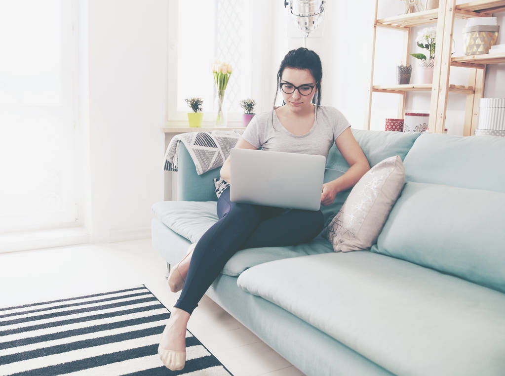 Jonge vrouw met laptop zittend op comfortabele sofa, home - Foto, afbeelding