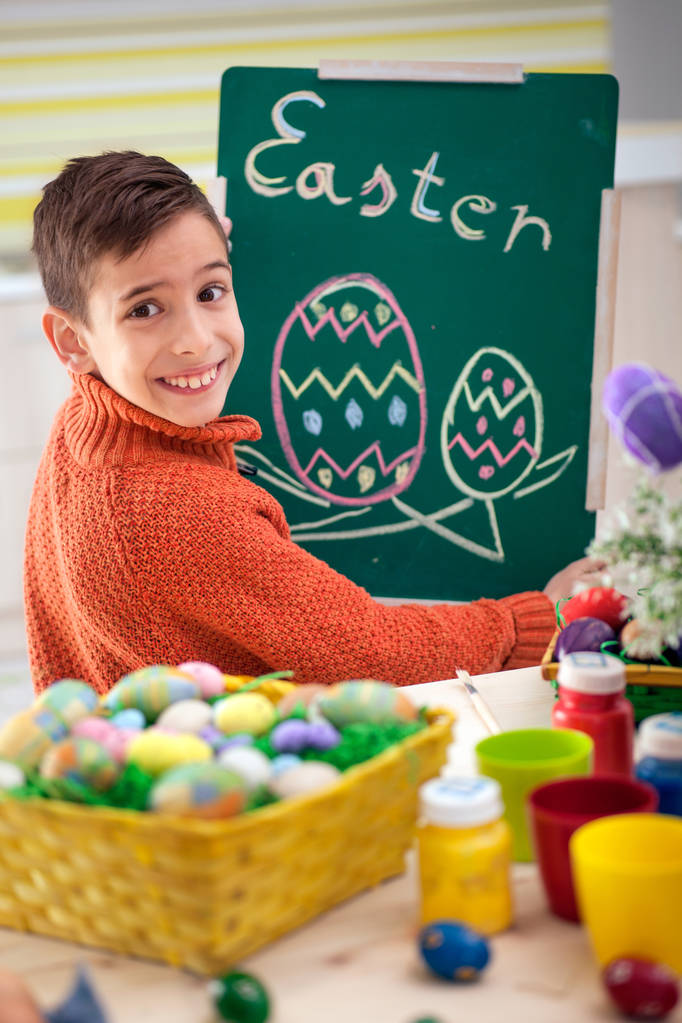 boy gülümseyerek Paskalya yumurtaları tebeşir ile yeşil kara tahta çizer. - Fotoğraf, Görsel