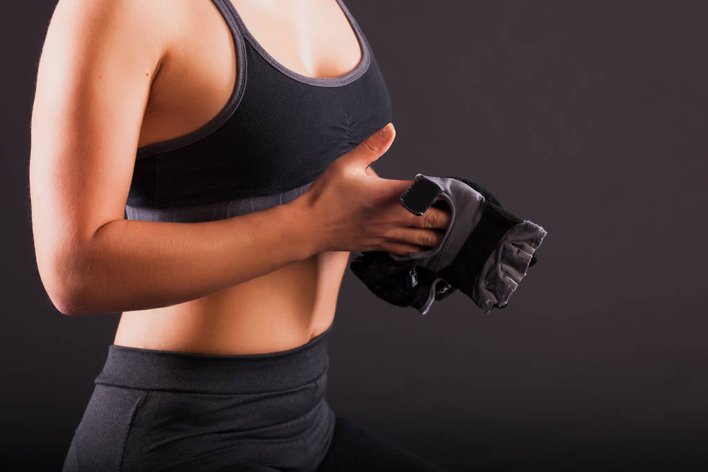 Una chica se pone guantes negros en las manos para un primer plano de fitness
 - Foto, Imagen