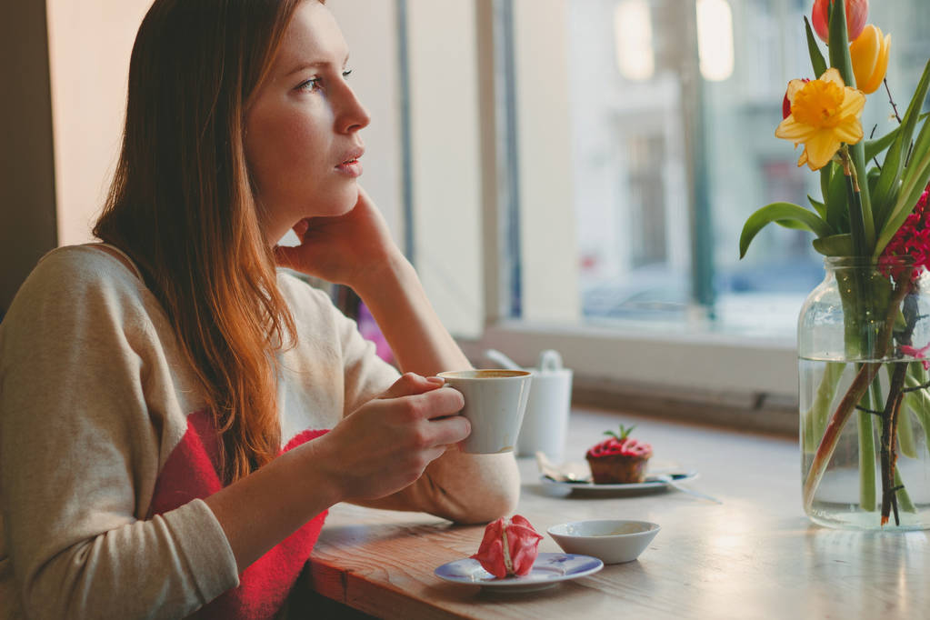 Красивая молодая женщина пьет кофе в кофейне у окна
 - Фото, изображение