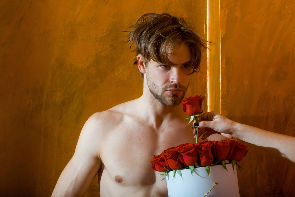bebaarde gespierde man met sexy lichaam houdt rood rose vak - Foto, afbeelding