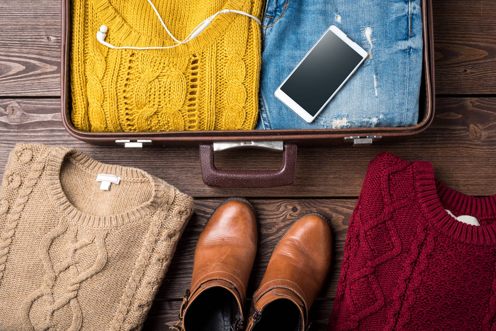 Ανοιχτό βαλίτσα με casual γυναικεία χειμερινά ρούχα στο ξύλινο τραπέζι. - Φωτογραφία, εικόνα