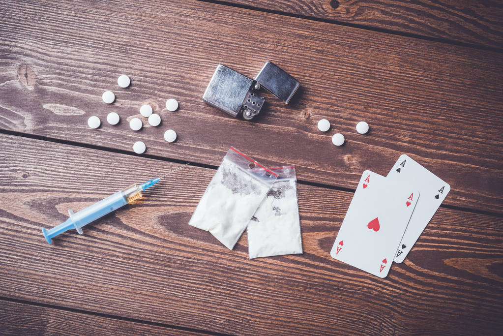 Hard drugs with pills, playing cards and syringe on wooden table - Photo, Image