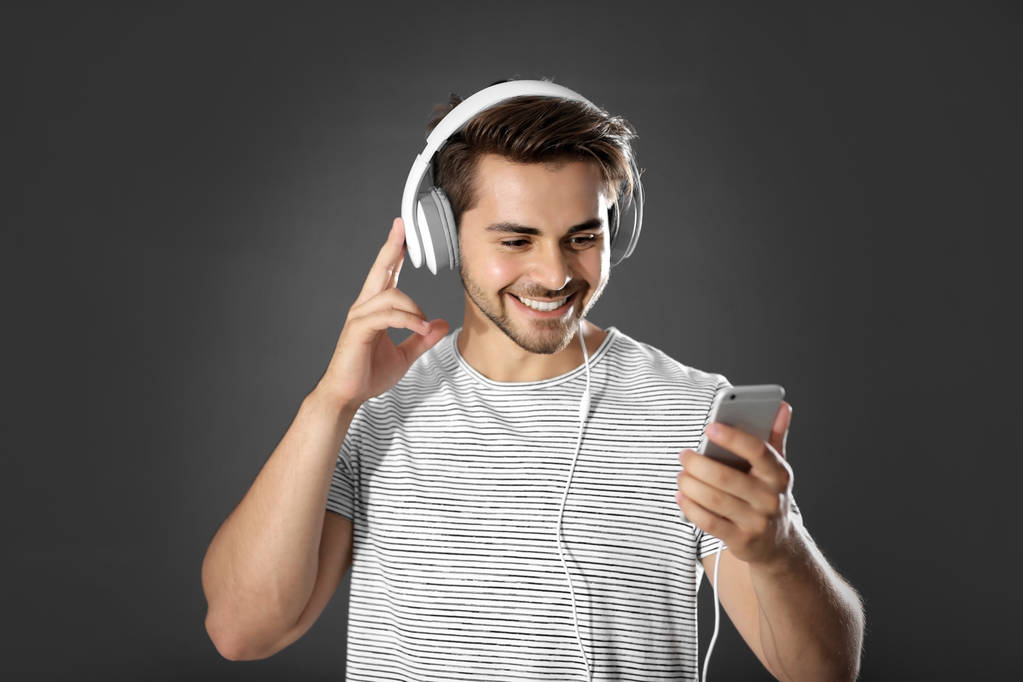 Emotional man with headphones listening music on grey background - Photo, Image