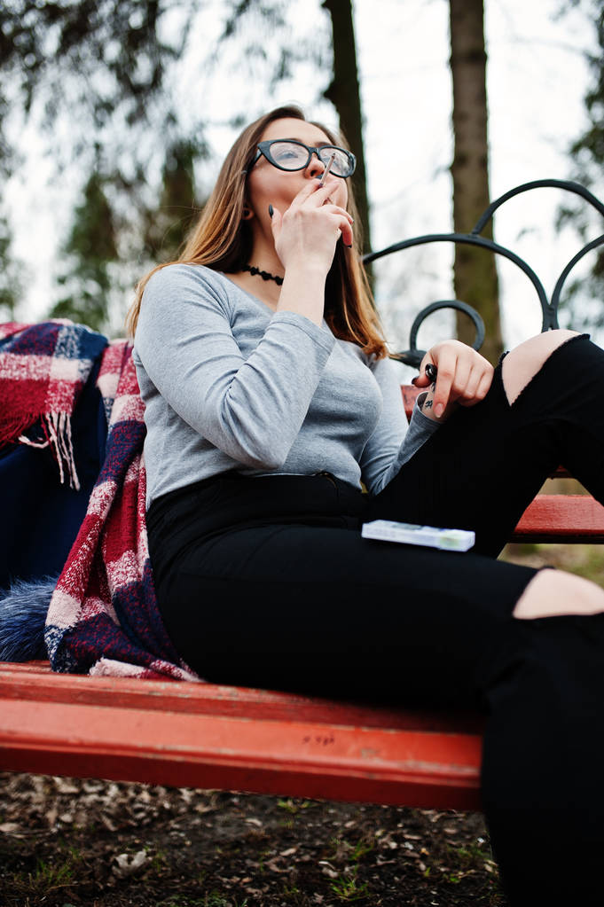 少女屋外のベンチに座ってタバコを吸っています。コンセプト  - 写真・画像