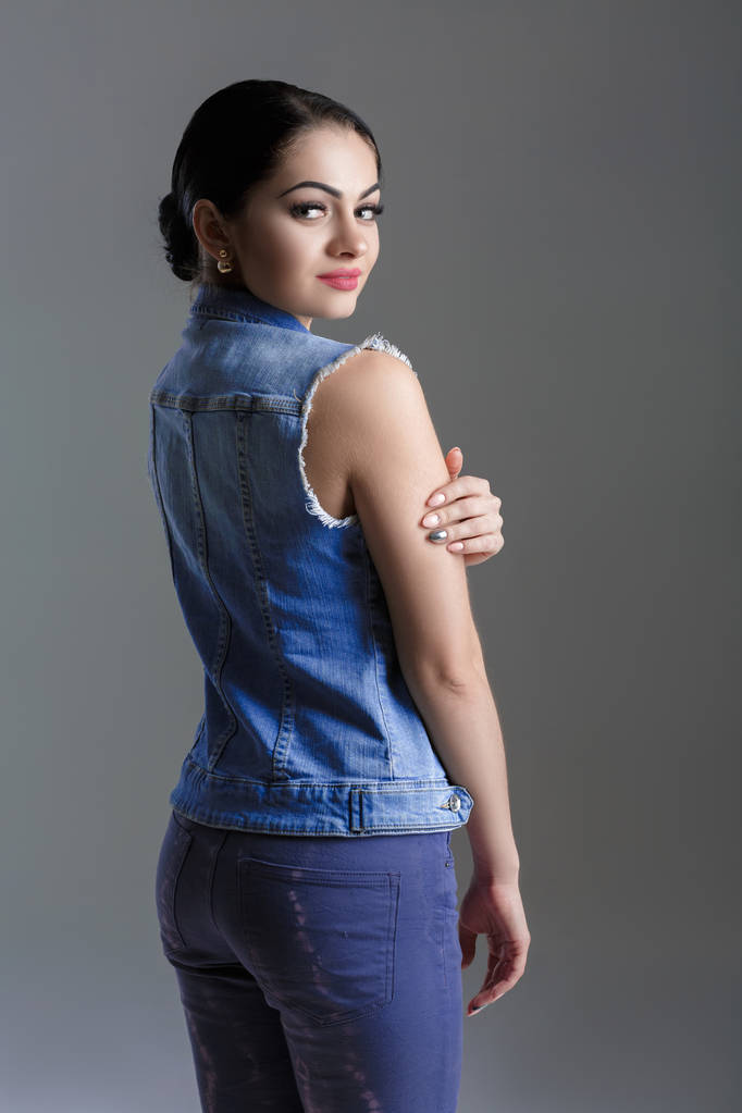 portrait of sexy young brunette woman in denim vest on grey background. - Photo, Image