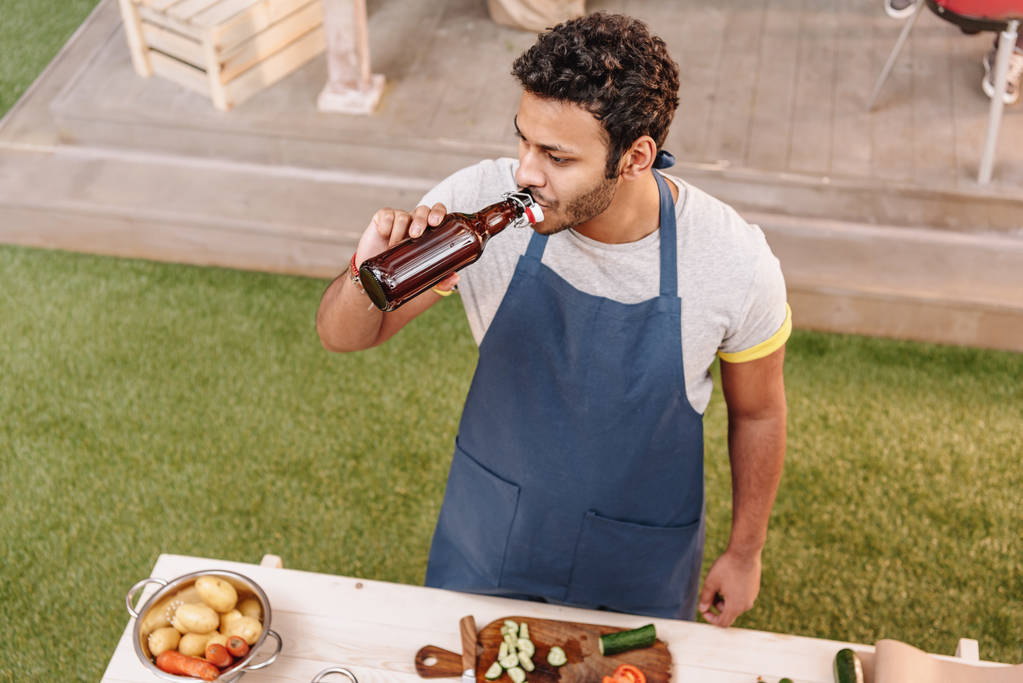 man making burgers and drinking beer from bottle outdoors - Photo, Image