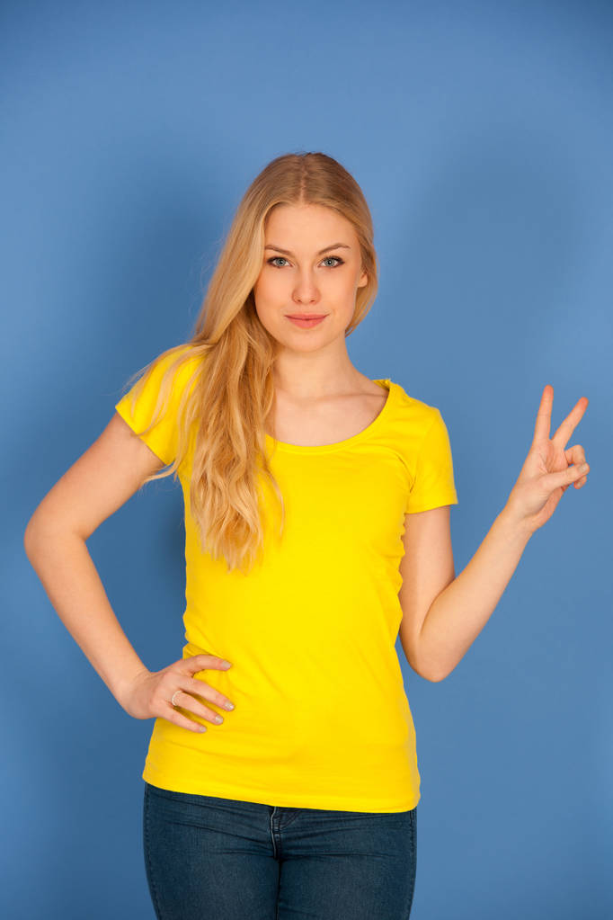 mladá blond žena v žluté t košile gesta vítězství ukazuje v  - Fotografie, Obrázek