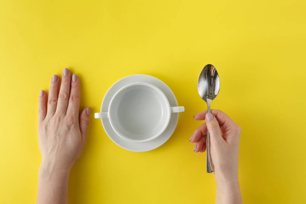 Empty white plate on yellow background with hands and spoon. Sou - Photo, Image