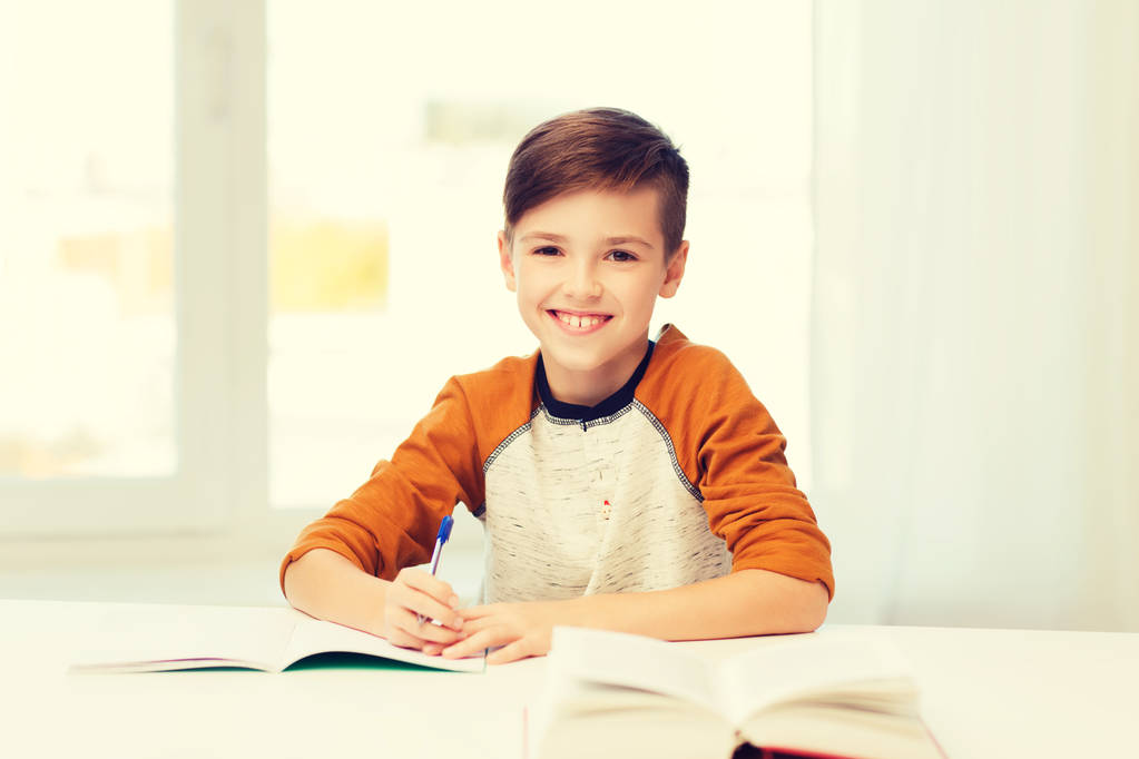 smiling student boy writing to notebook at home - Photo, Image
