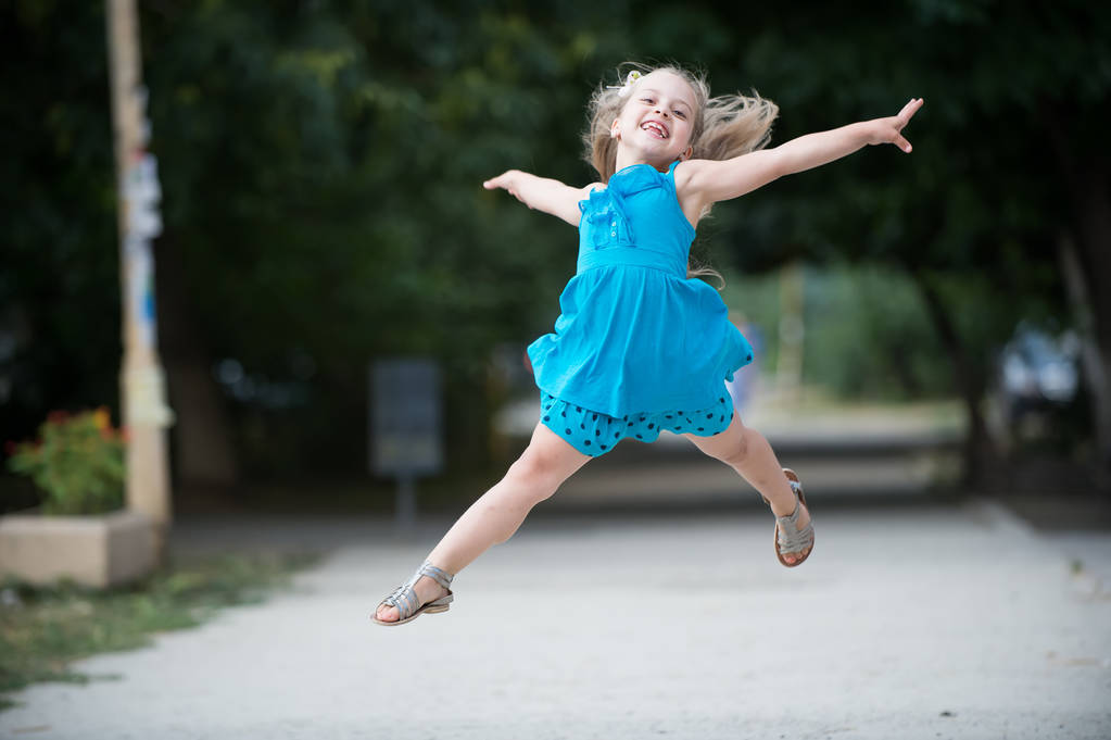 mała dziewczynka z uśmiechniętą twarz skoki w niebieskiej sukience - Zdjęcie, obraz