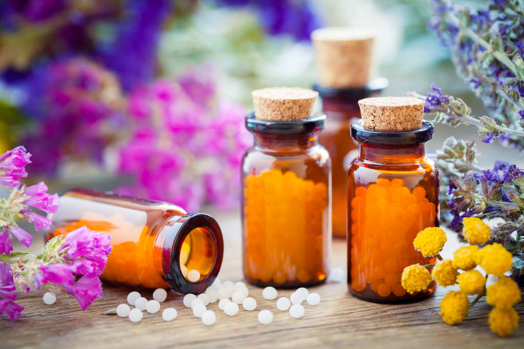 Flessen van homeopathische bolletjes, mortel, healing kruiden en bloemen. - Foto, afbeelding
